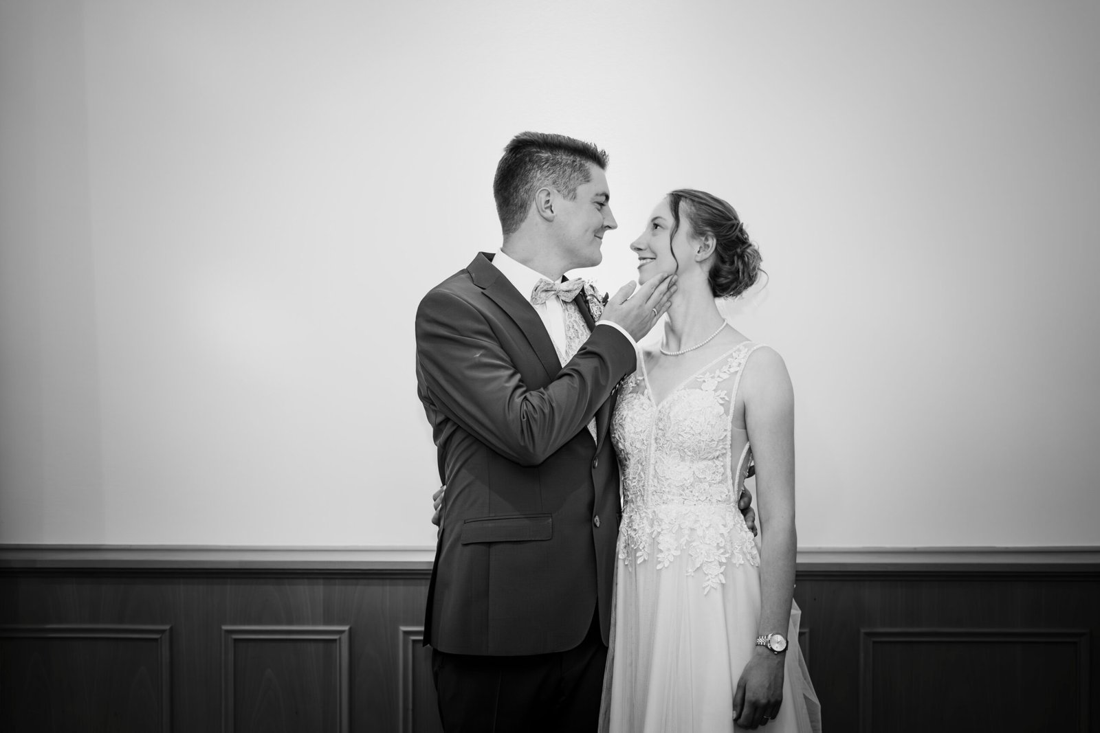 Schwarz-Weiß-Portrait eines glücklichen Brautpaares am Hochzeitstag. Der Bräutigam berührt zärtlich das Gesicht der Braut, während sie sich liebevoll in die Augen schauen. Professionelles Hochzeitsfoto aus Osnabrück.