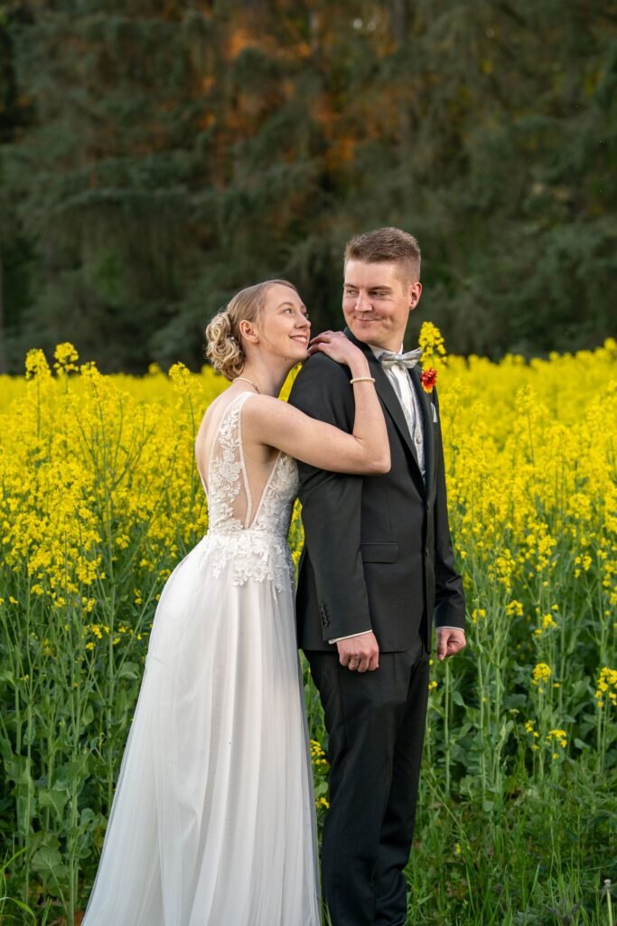 Braut lehnt ihren Kopf zärtlich an die Schulter des Bräutigams beim Paarshooting im gelben Rapsfeld in Bissendorf. Natürliche Hochzeitsfotografie in der Region Osnabrück von Mirovisuals.