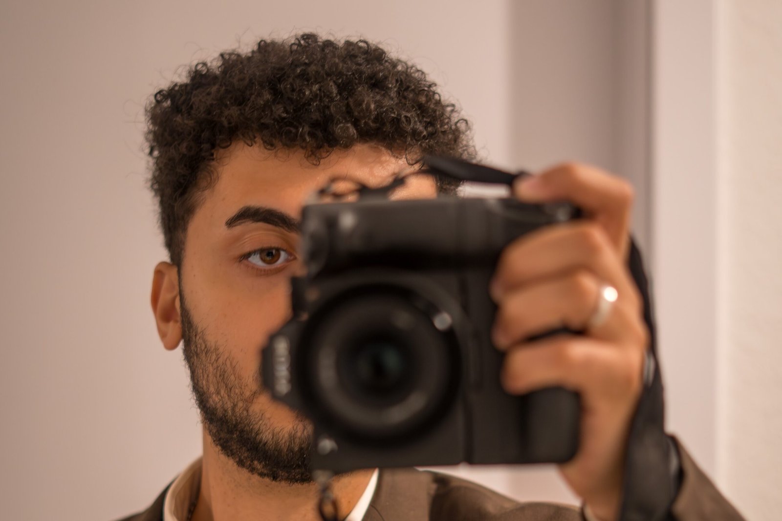 Portrait von Mirovisuals, dem Hochzeits- und Eventfotografen aus Osnabrück. Er trägt einen eleganten braunen Anzug mit roter Krawatte und fotografiert sich selbst im Spiegel mit einer Sony-Kamera.