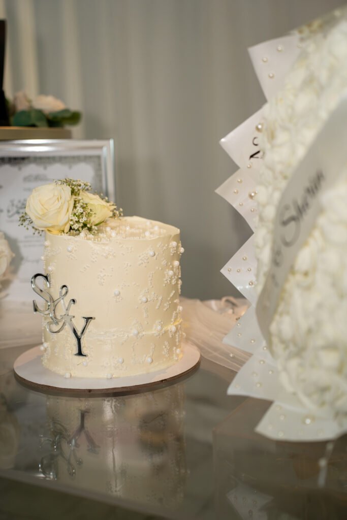 Elegante weiße Hochzeitstorte mit Perlenverzierung, weißen Rosen und silbernem S&Y-Topper, fotografiert auf einer Feier in Osnabrück.